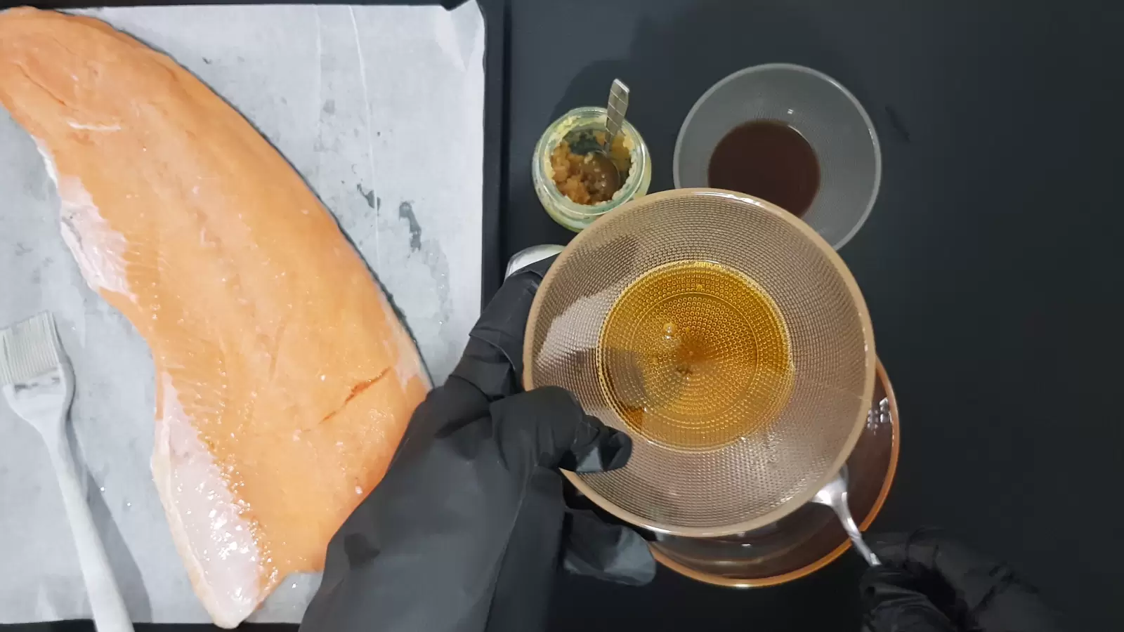 Bowl with honey, bowl with soy, jar of crushed garlic, baking dish with salmon and brush