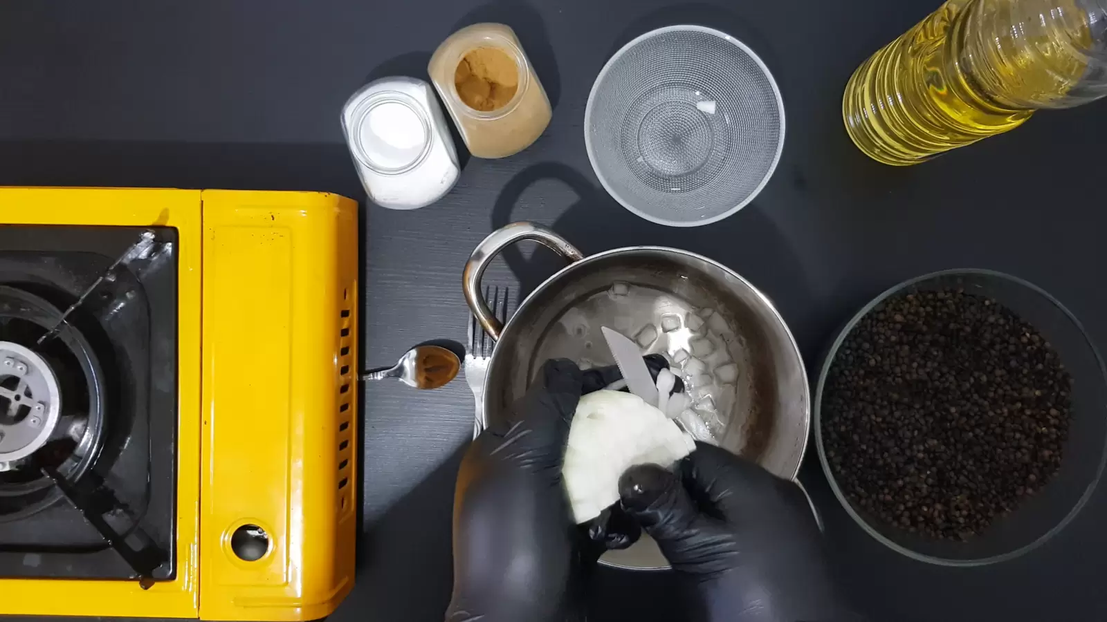 Bowl with lentils, empty bowl, jar of cumin, jar of salt, bottle of oil, gas jar, pot, knife cutting onion and spoon