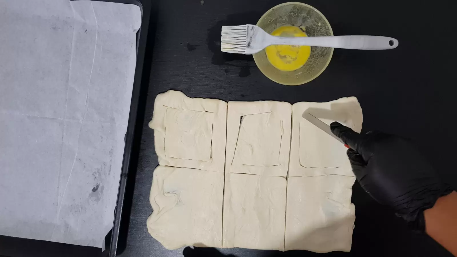 Puff pastry cut into 6 cubes and a cutting knife, bowl with egg and brush. Baking pan and baking paper.