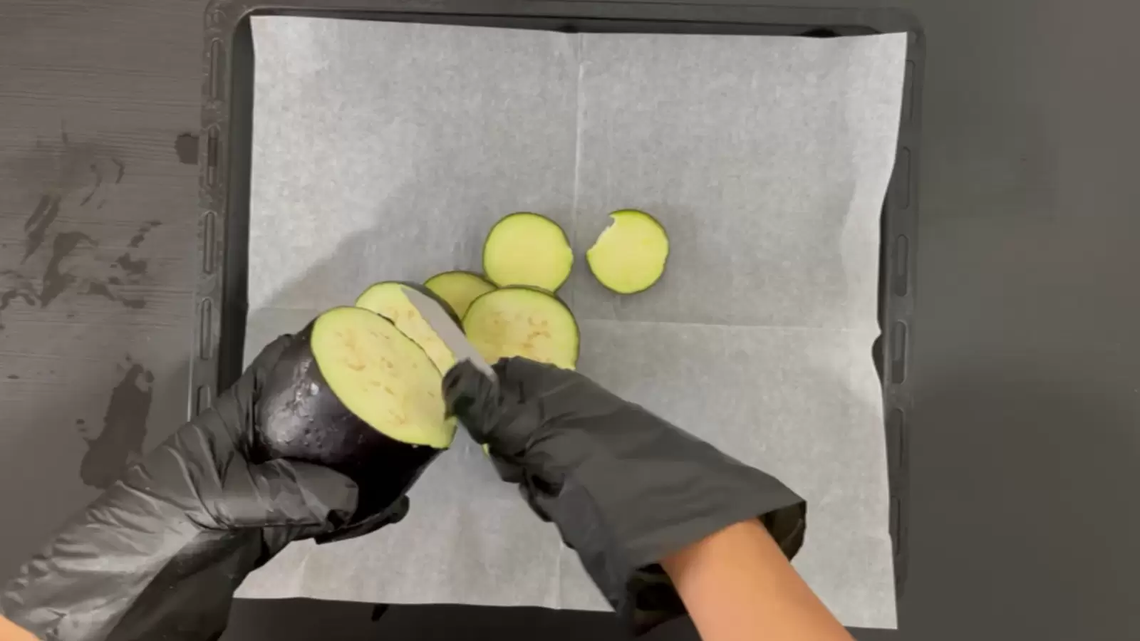 Baking sheet with baking paper, medium eggplant cut into slices.