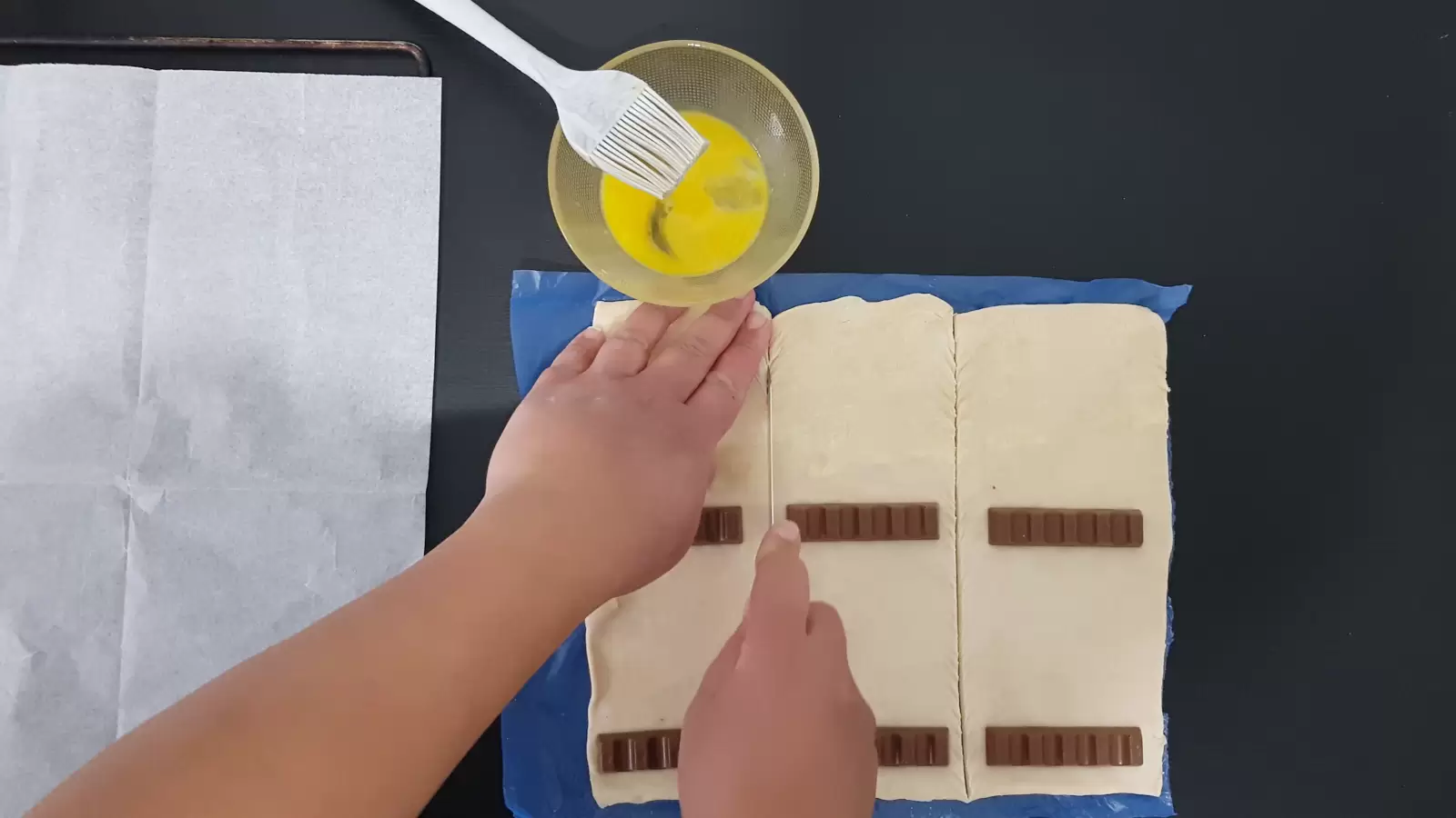 Six Kinder Buenos, a knife for cutting puff pastry, a bowl with an egg and a brush, baking paper in an oven tray