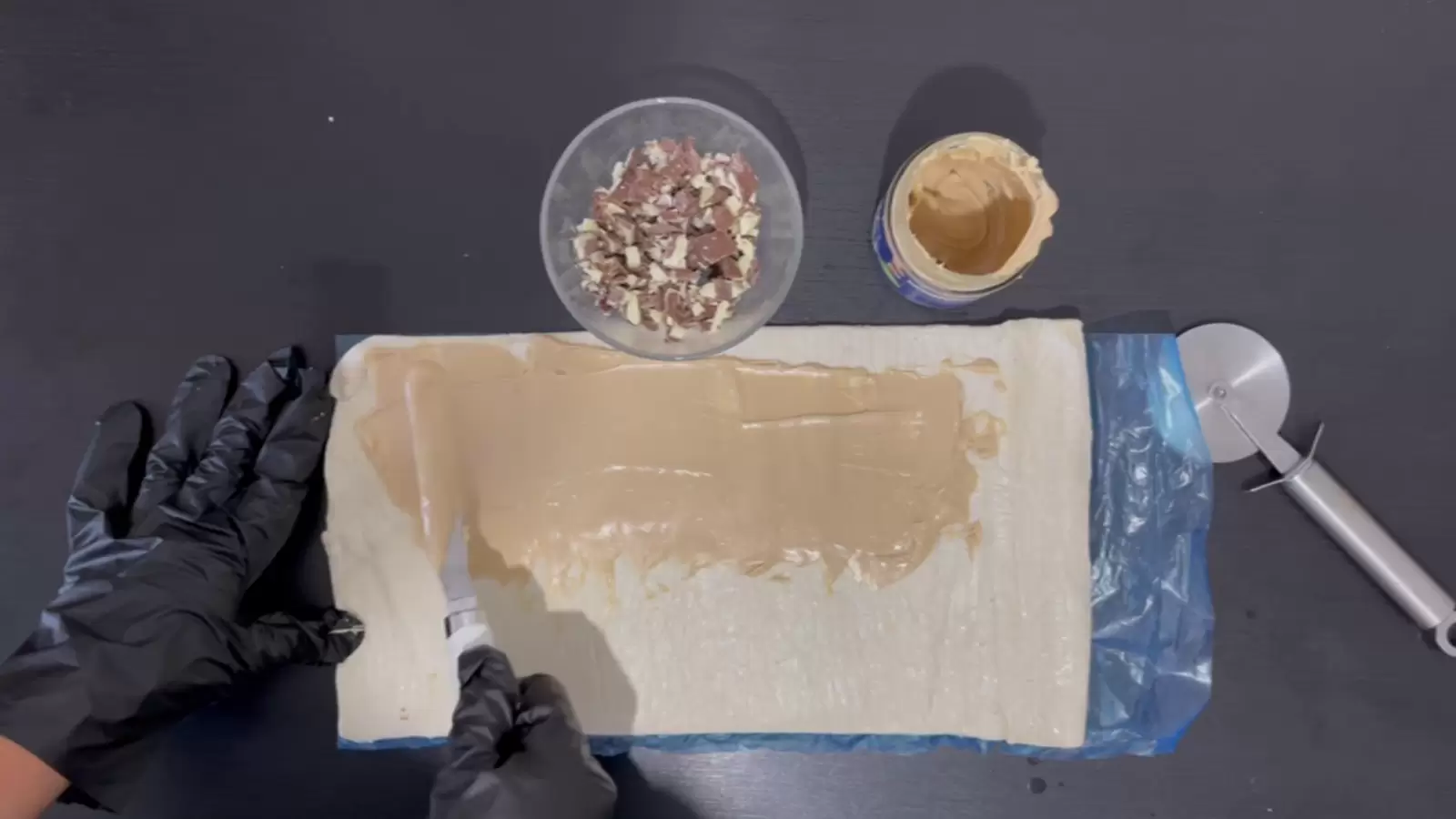 Pizza roller, Kinder Bueno spread, Kinder Bueno chopped in bowl, puff pastry spread with Kinder Bueno spread on top