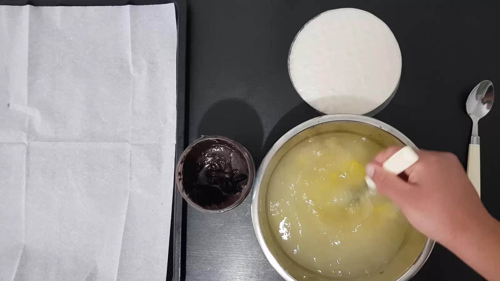 A fork in a bowl with water and eggs, a jar with chocolate, rice paper, a spoon, a baking sheet