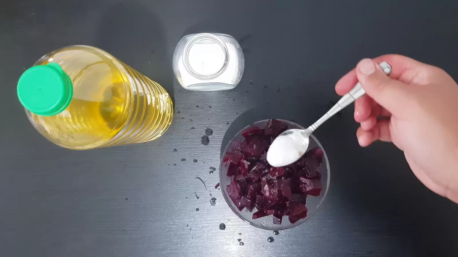 A jar of salt with a spoon, a bottle of olive oil, a bowl of beets