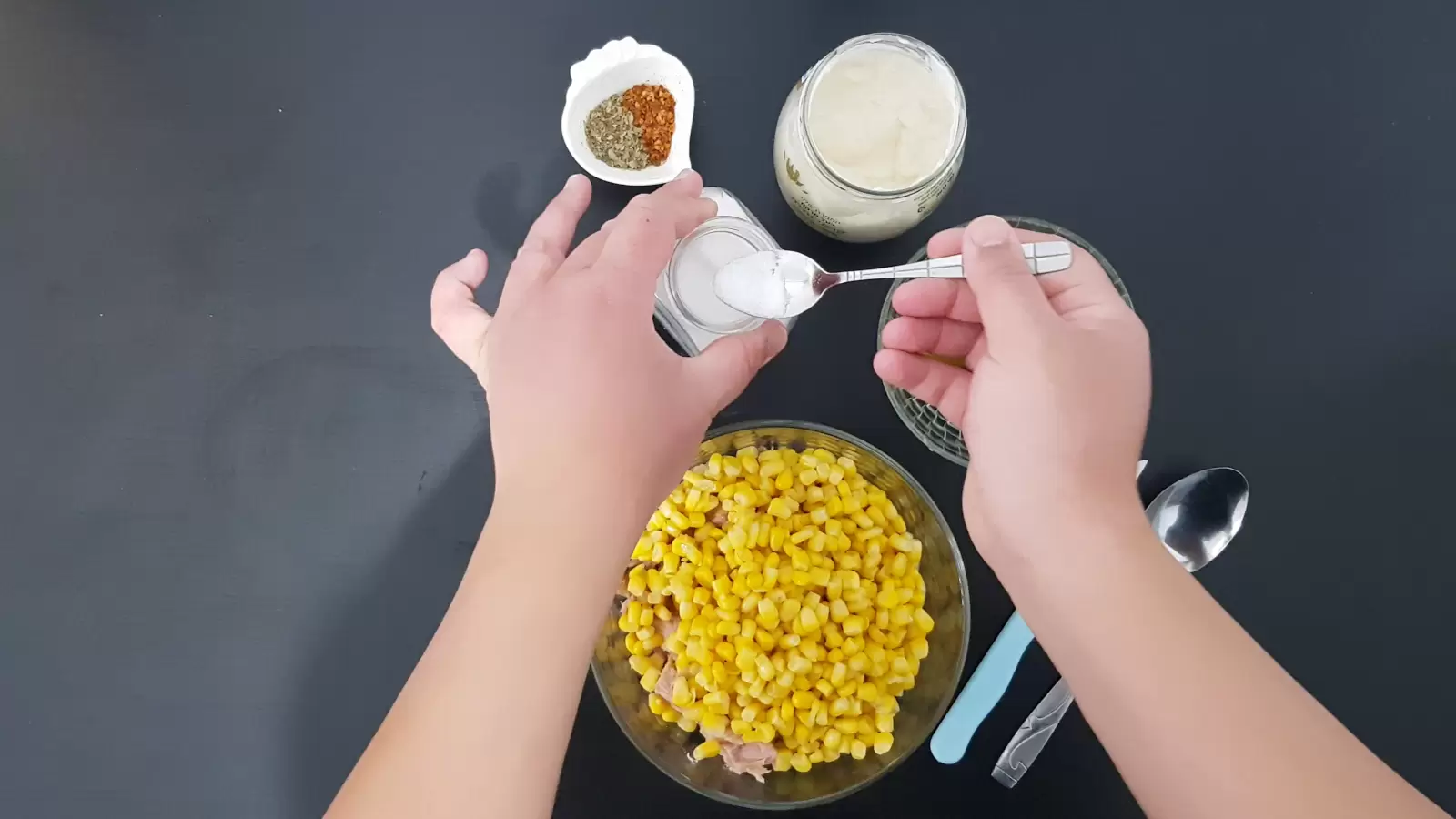 A jar of mayonnaise, a bowl with chili, a jar of salt and a spoon, a bowl with corn, a spoon