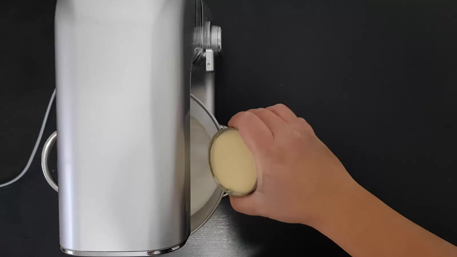 A can of condensed milk is poured into a bowl with whipping cream in a mixer