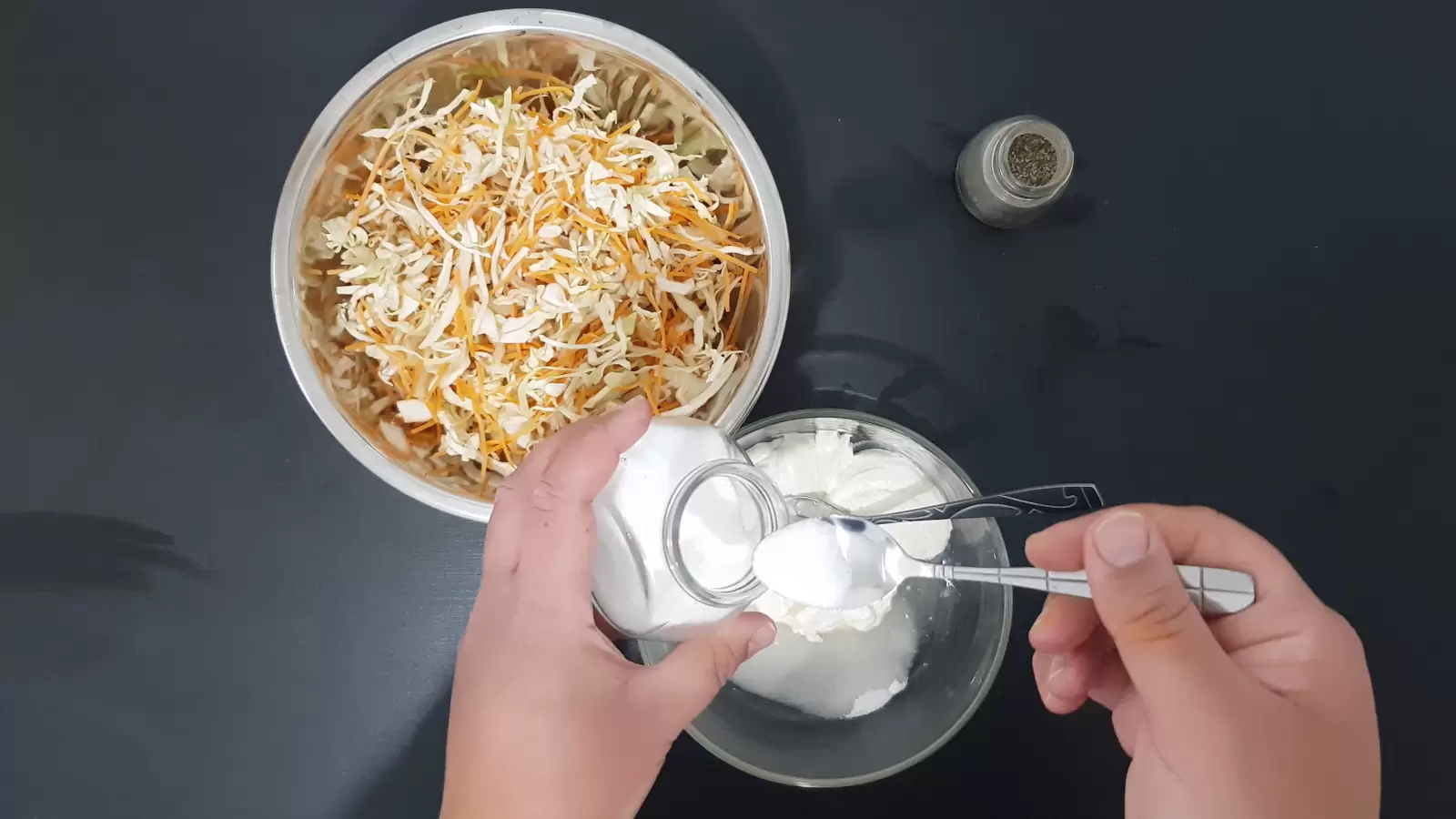 One bowl with cut carrots and cabbage, a second bowl with mayonnaise and sugar, a teaspoon of salt, a jar of pepper