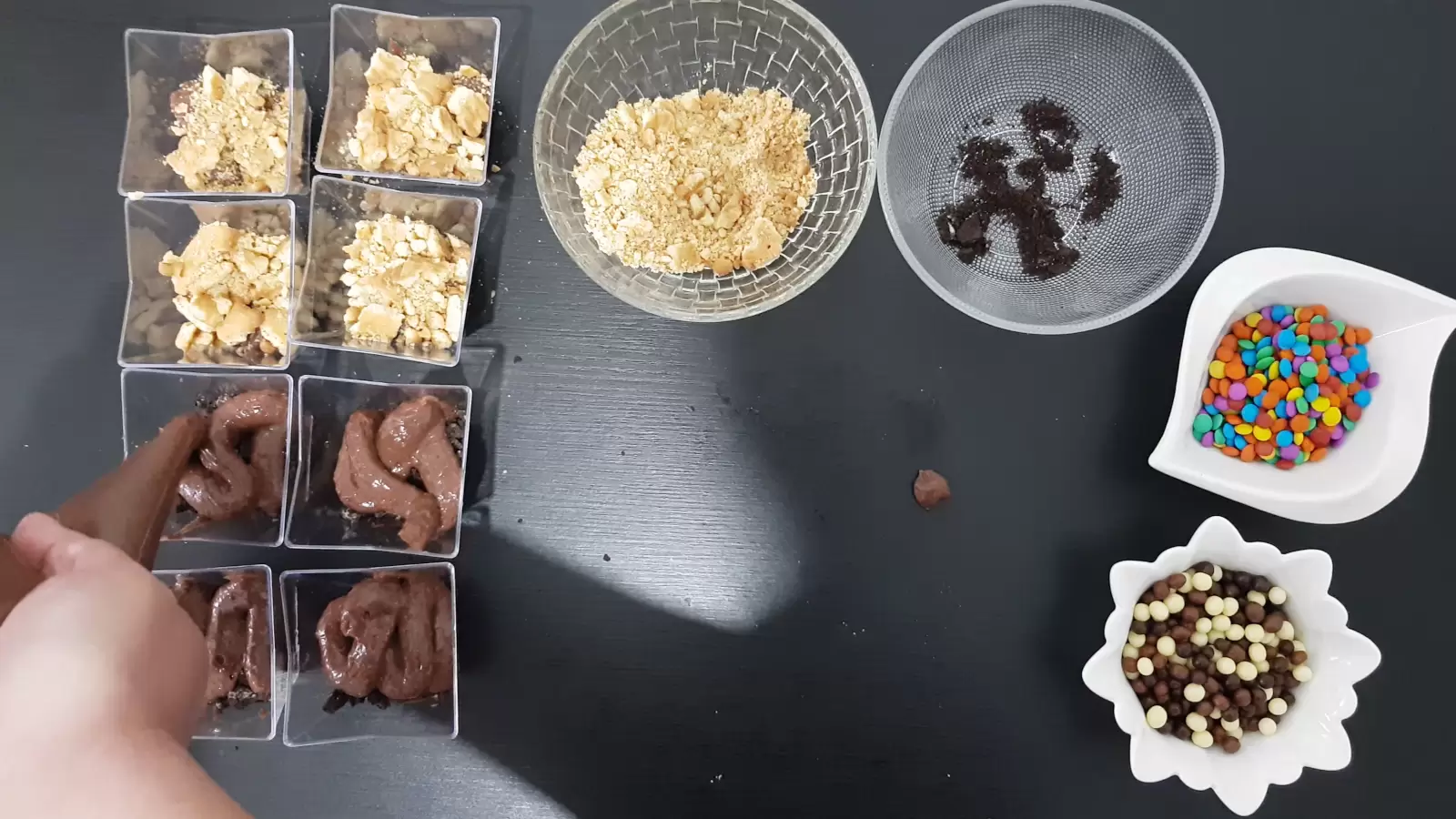 Dessert cups with cookie crumbs, bowl with biscuit crumbs and Oreo, piping bag with pudding, bowl with candies
