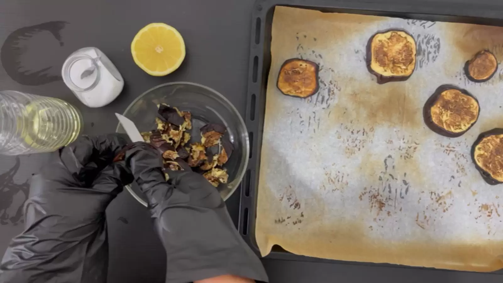 Baking sheet with baking paper, sliced eggplant, bowl with diced eggplant, half a lemon, jar of salt, bottle of oil