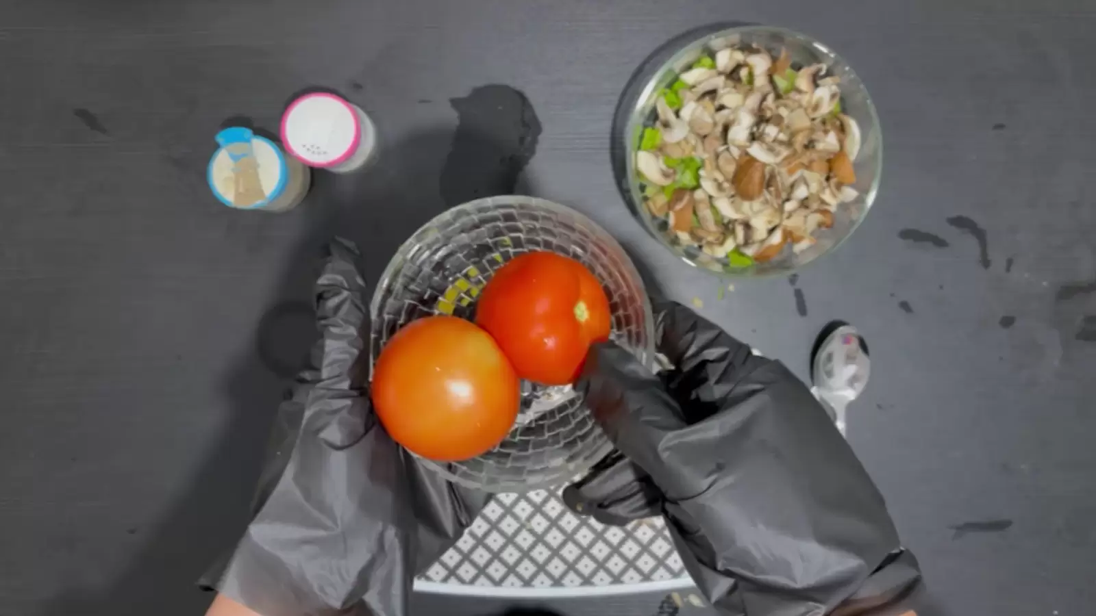 Bowl with lettuce and mushrooms, jar of salt, jar of pepper, cutting board, spoon, bowl with tomatoes