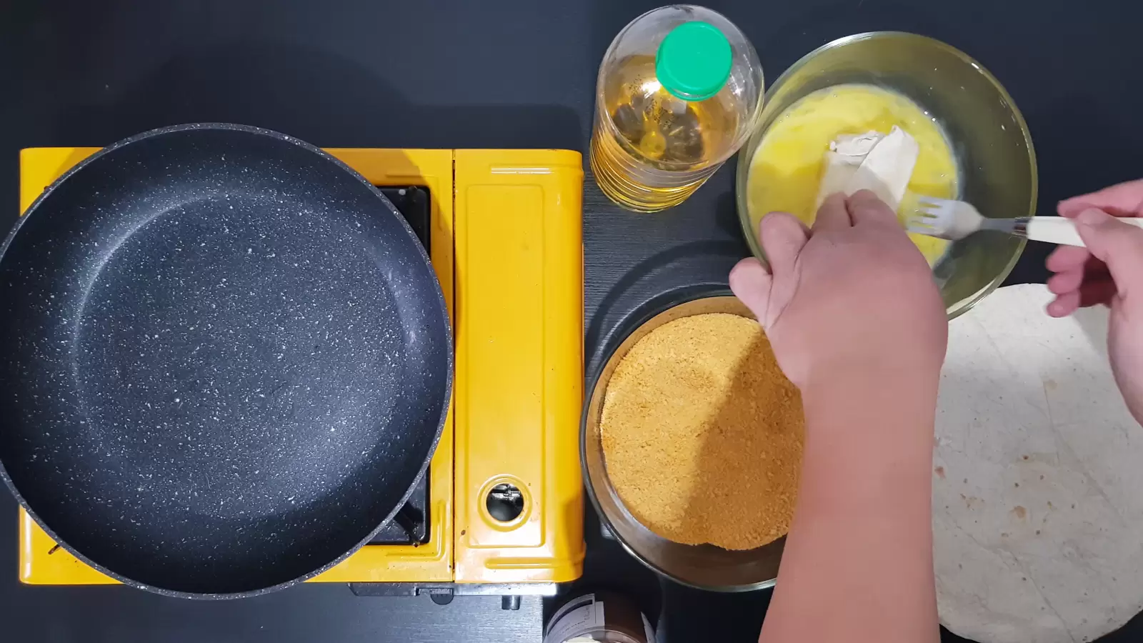 Chocolate-filled tortilla in bowl with egg, bottle of oil, bowl with breadcrumbs, stove and frying pan