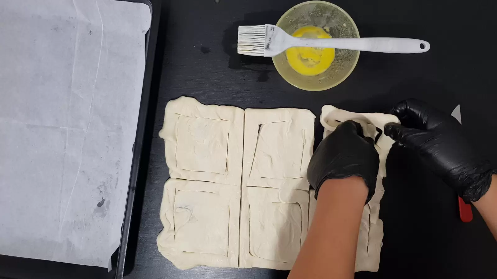 Puff pastry cut into 6 cubes, one cube folded from one side to the other, bowl with egg and brush. Baking pan and baking paper.