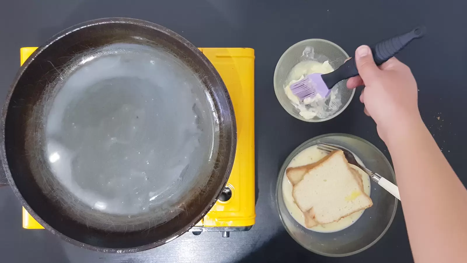 2 slices of bread, bowl with butter and brush for brushing, bowl with batter and dipped slices of bread, fork, frying pan