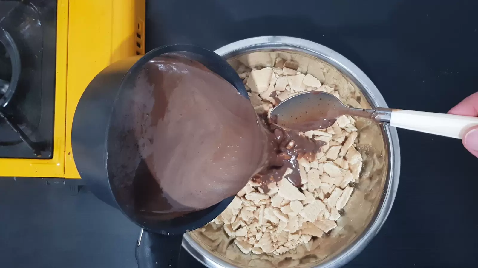 A bowl with biscuits, a pot with chocolate mixture poured into it, a spoon