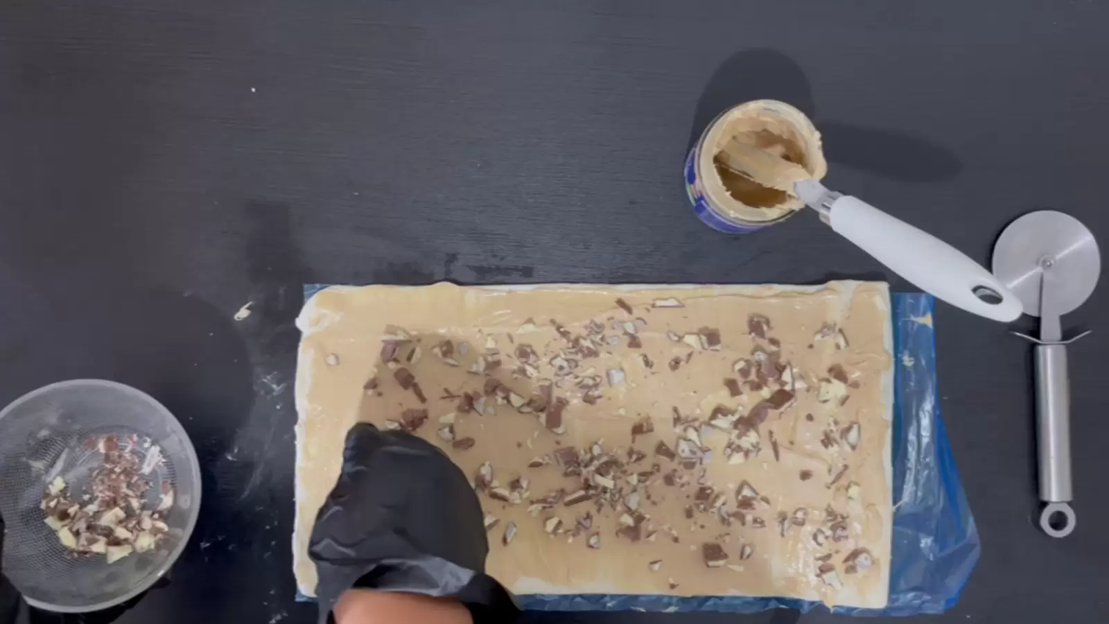 Pizza roller, Kinder Bueno spread with knife, open puff pastry with Kinder Bueno on top, bowl of chopped Kinder Bueno