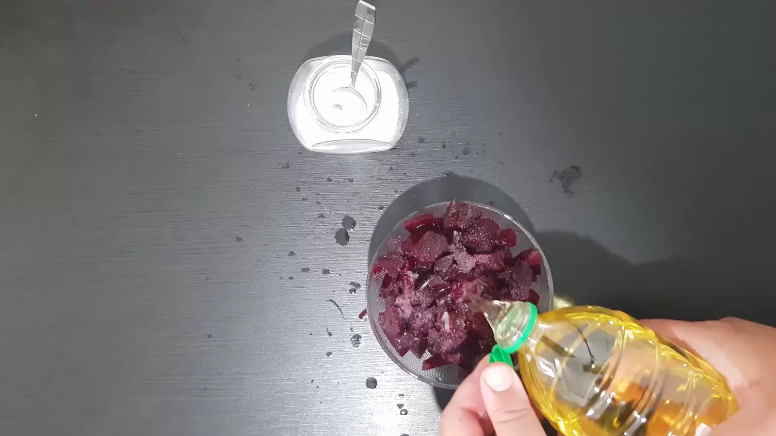 A jar of salt with a spoon, a bottle of olive oil poured into a bowl of beets