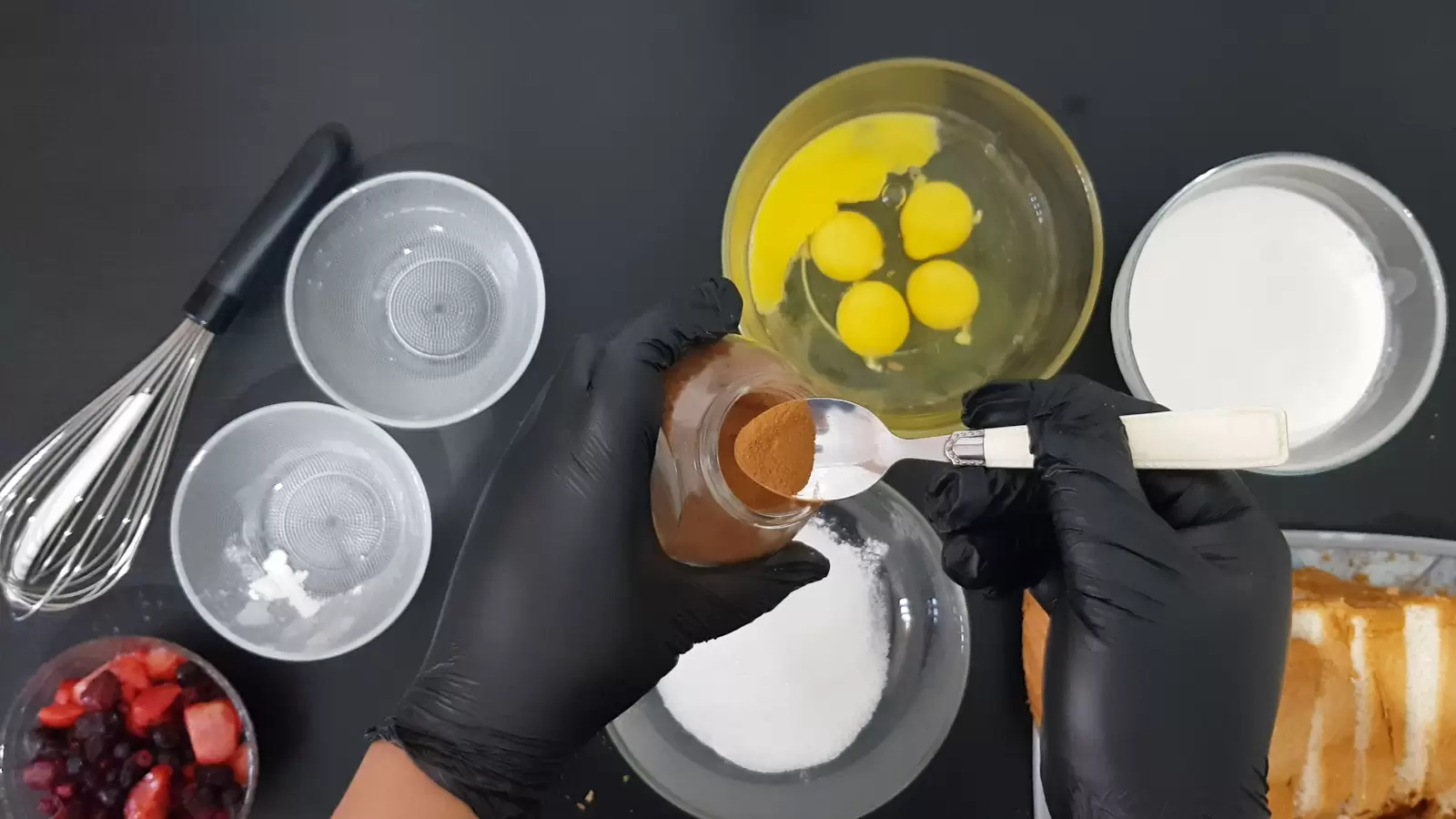 Bowl of heavy cream, bowl of eggs, 2 empty bowls, bowl of berries, sliced ​​bread on cutting board, whisk, jar of cinnamon spice and spoon over bowl of sugar