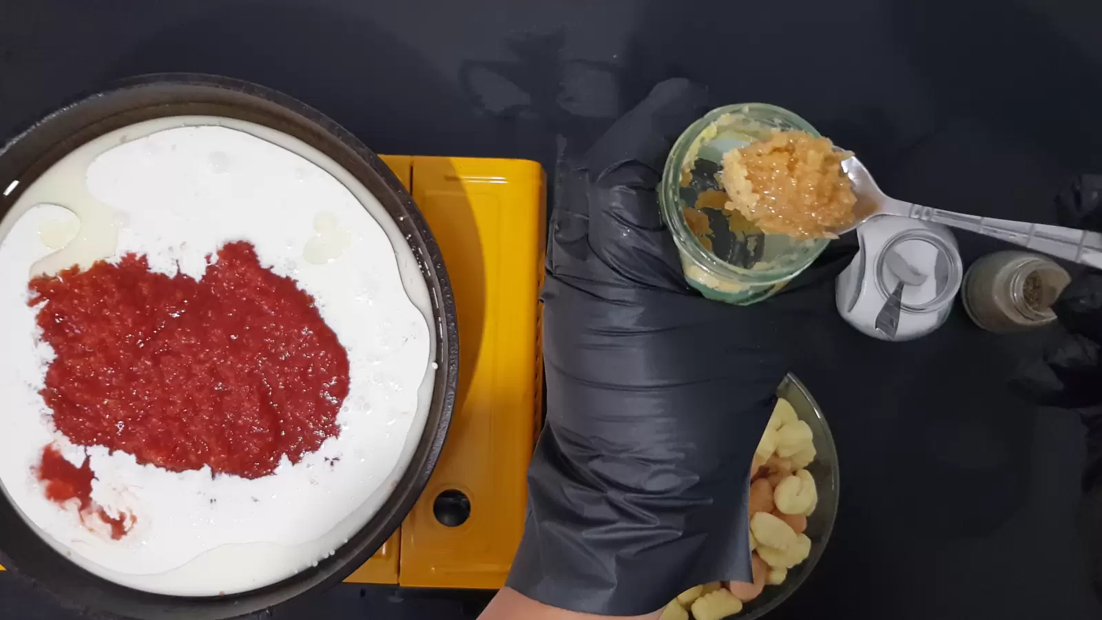 a spoon of crushed garlic and a jar, a jar of salt and a spoon, a jar of pepper, a frying pan with whipping cream and crushed tomatoes
