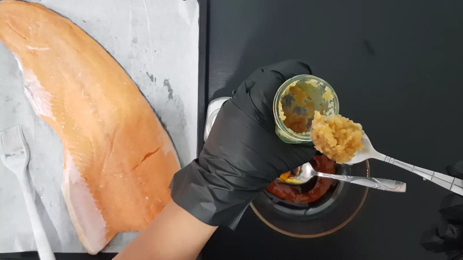 jar of crushed garlic, bowl with sauce, baking dish with salmon and brush