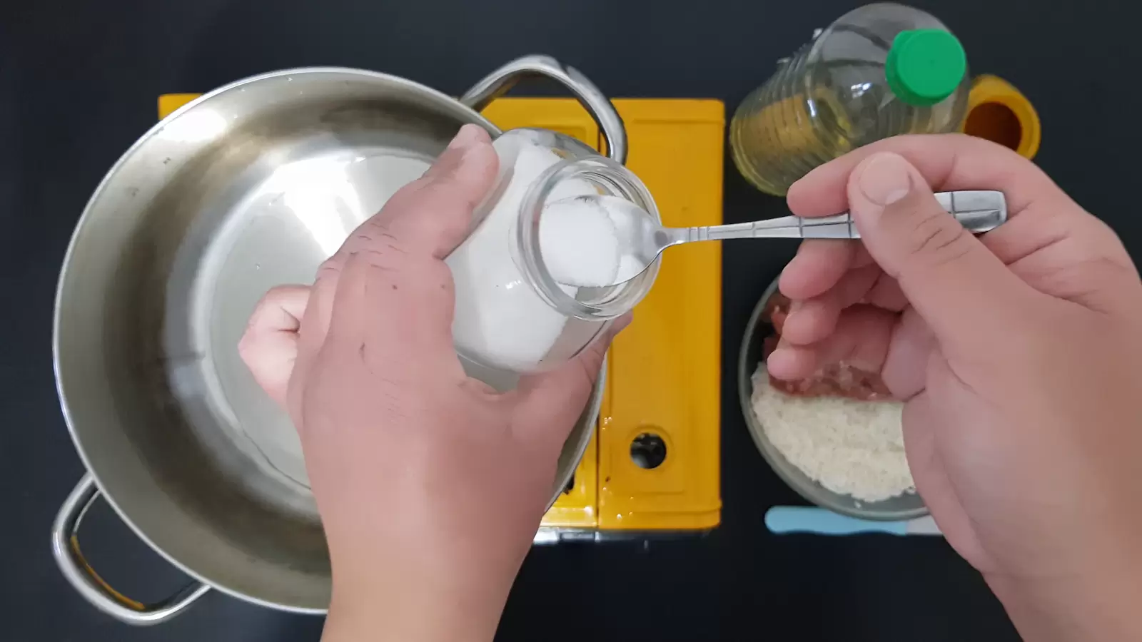 Oil, a bowl with rice, a knife, a jar of salt with a spoon, a pot