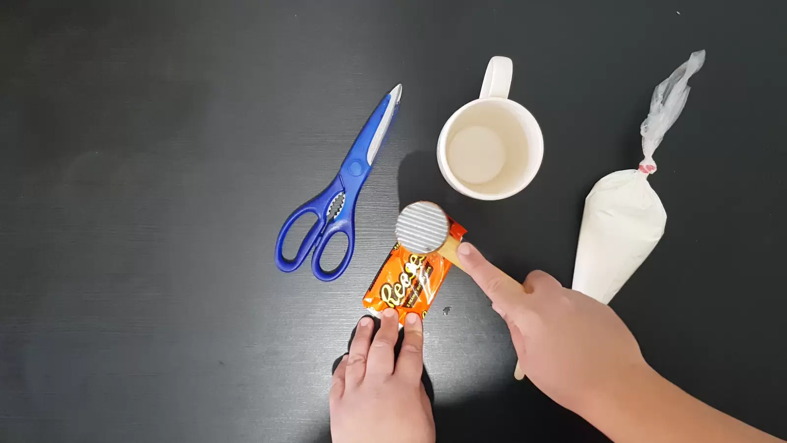Sweet cream in a piping bag, mug, scissors, kitchen hammer on a Reeses package