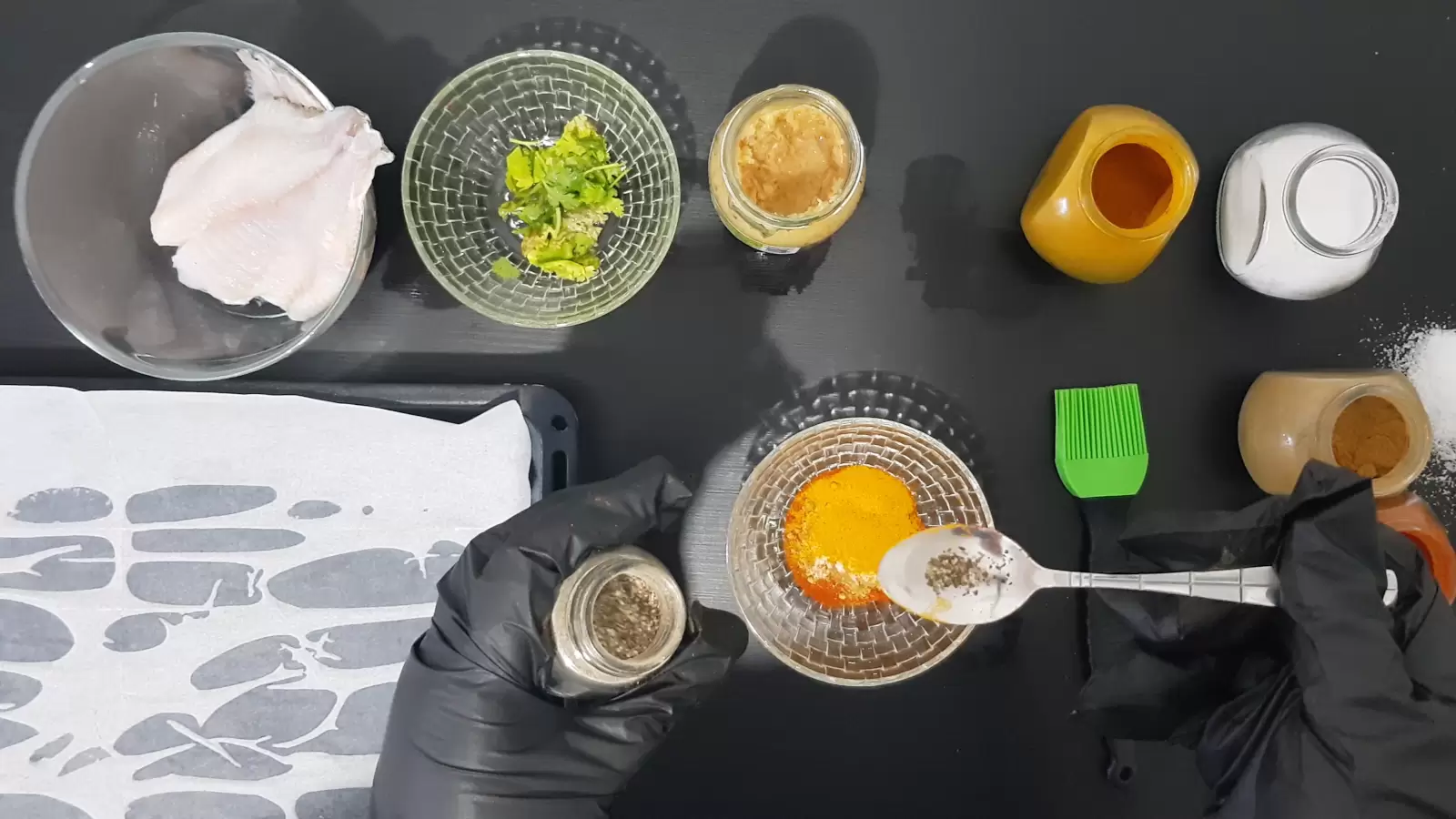 Turmeric, cumin, salt, garlic, coriander, oven tray, tilapia fish, and a teaspoon with pepper