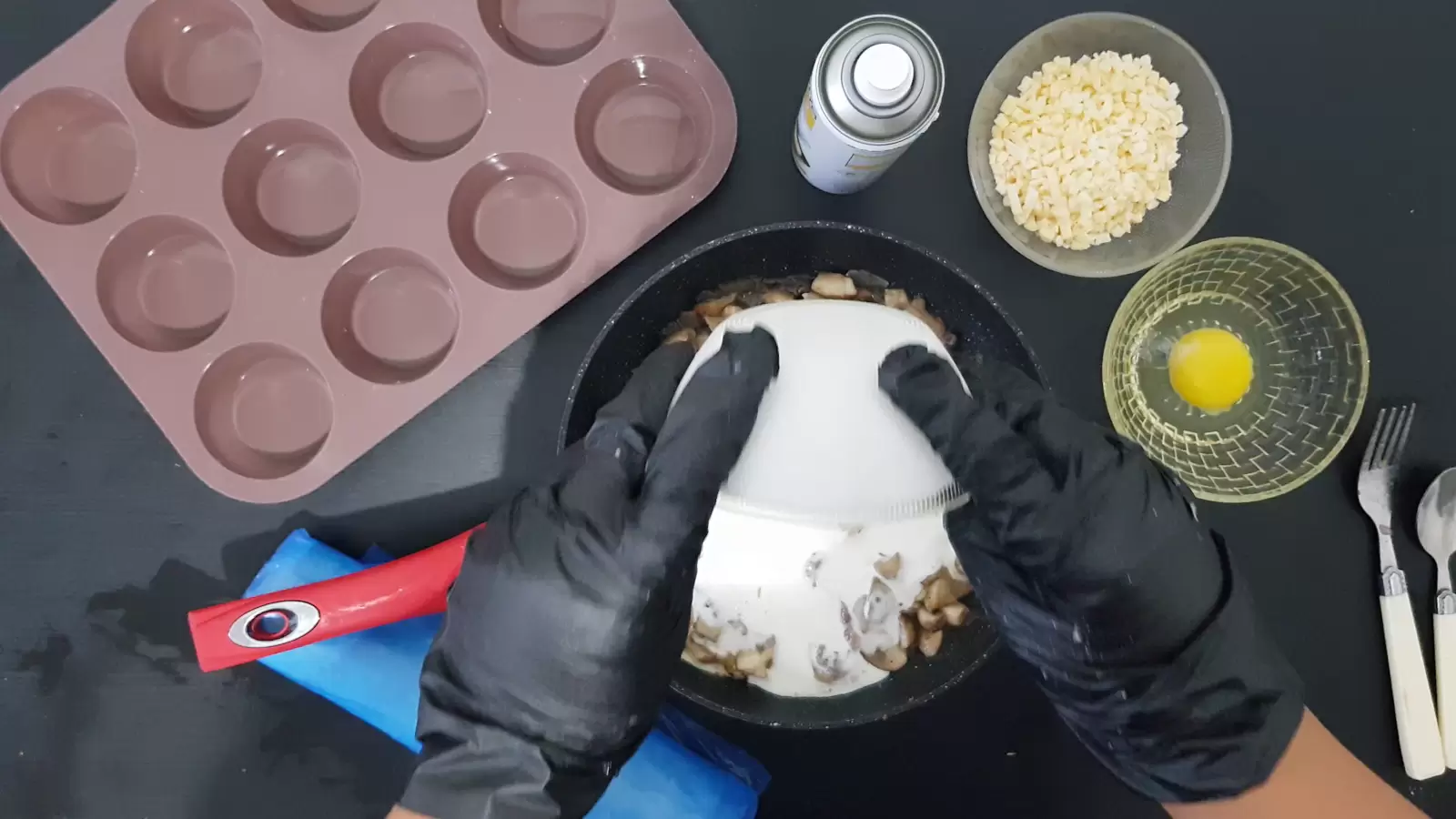 Bowl with grated cheese, bowl with egg, oil spray, pan with mushrooms and cream poured into it, muffin tin, rolled filo dough