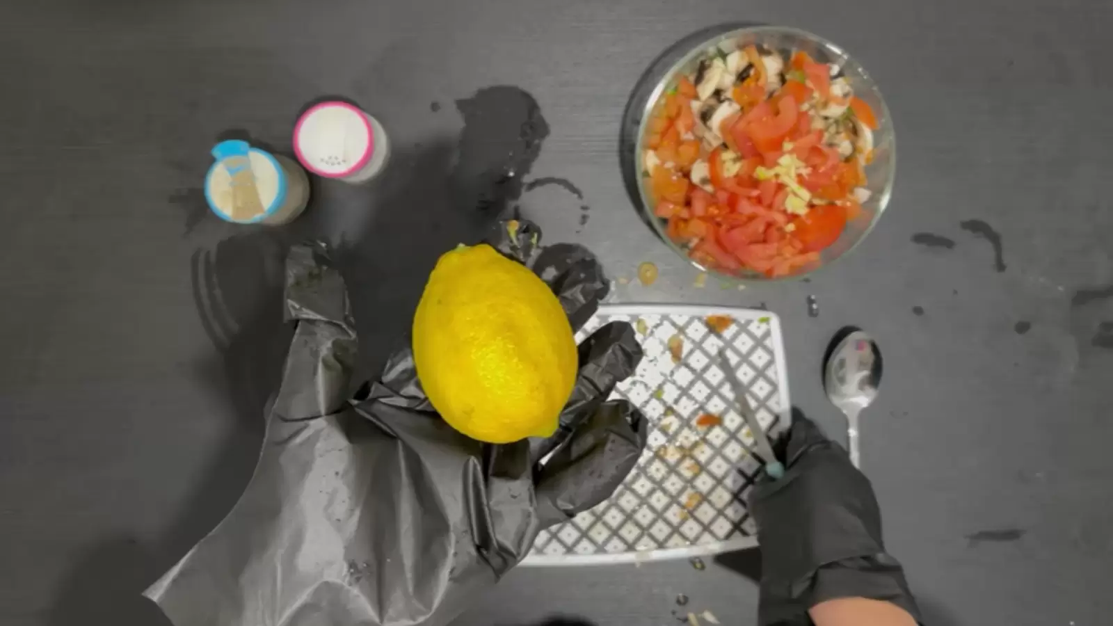 Bowl with lettuce, tomato and mushrooms, jar of salt, jar of pepper, cutting board, spoon, lemon