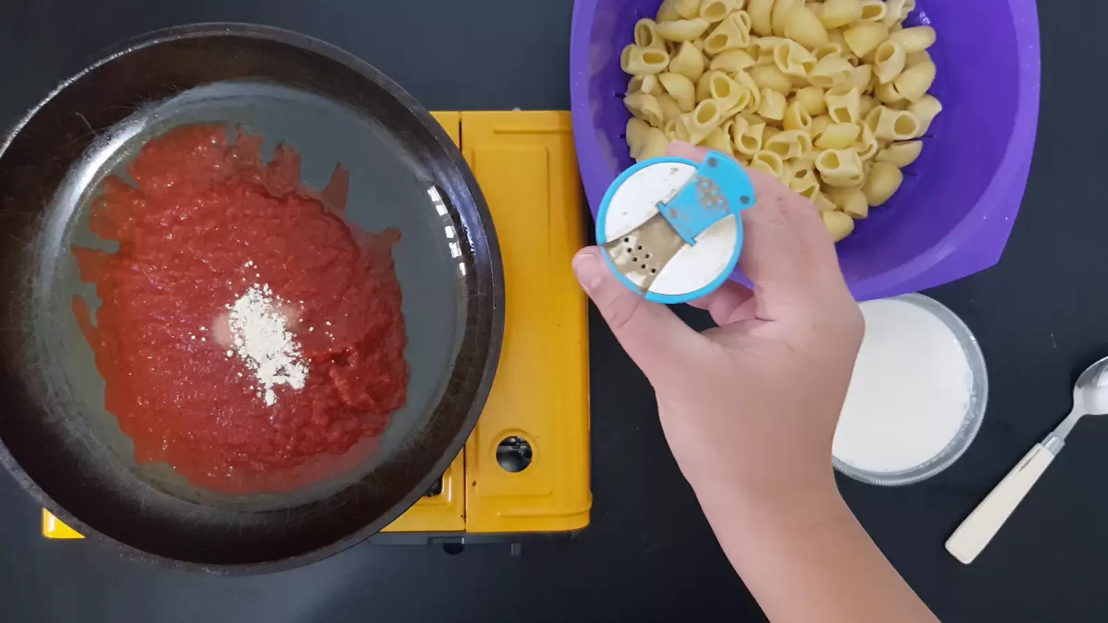 Bowl with pasta, pan with crushed tomatoes, jar of black pepper, spoon, bowl with whipped cream