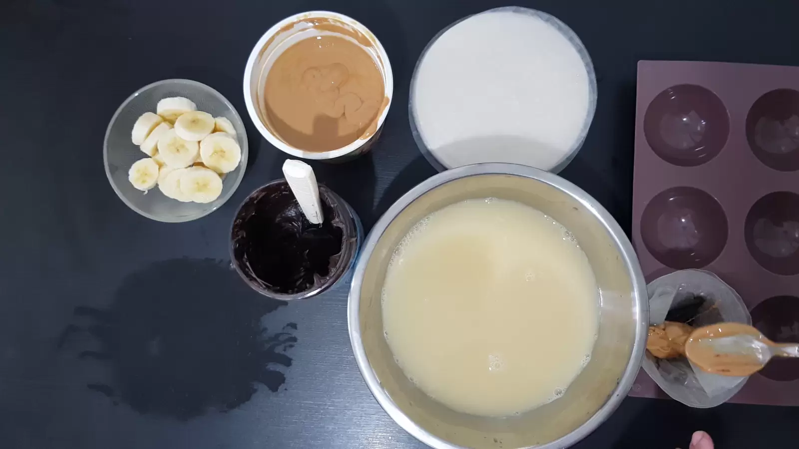 Rice paper in muffin pan with peanut butter spoon, rice paper, peanut butter jar, chocolate jar, bowl of sliced ​​bananas, Large bowl with mixture