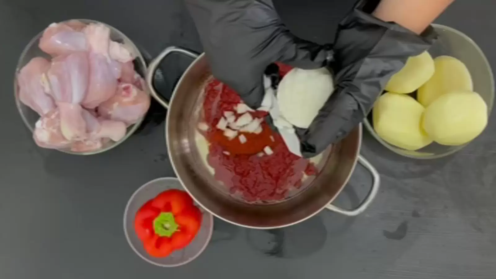 A bowl with chicken thighs, a bowl with red pepper, a bowl with 4 potatoes, a pot, an onion and a knife