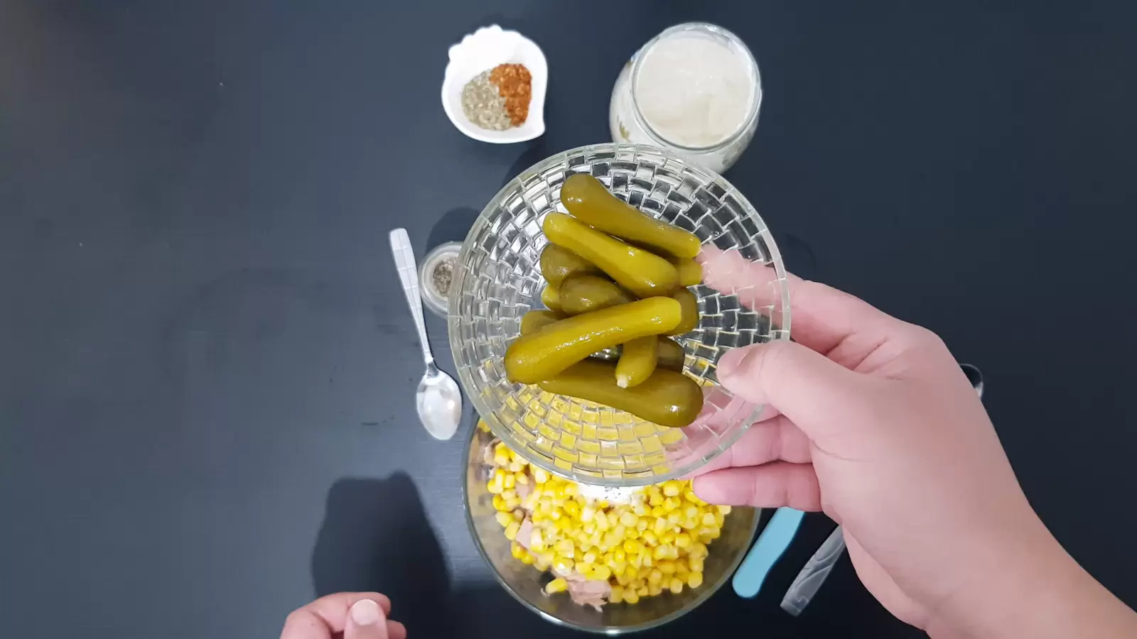 Bowl with pickles, jar of mayonnaise, bowl with chili, bowl with corn, spoon