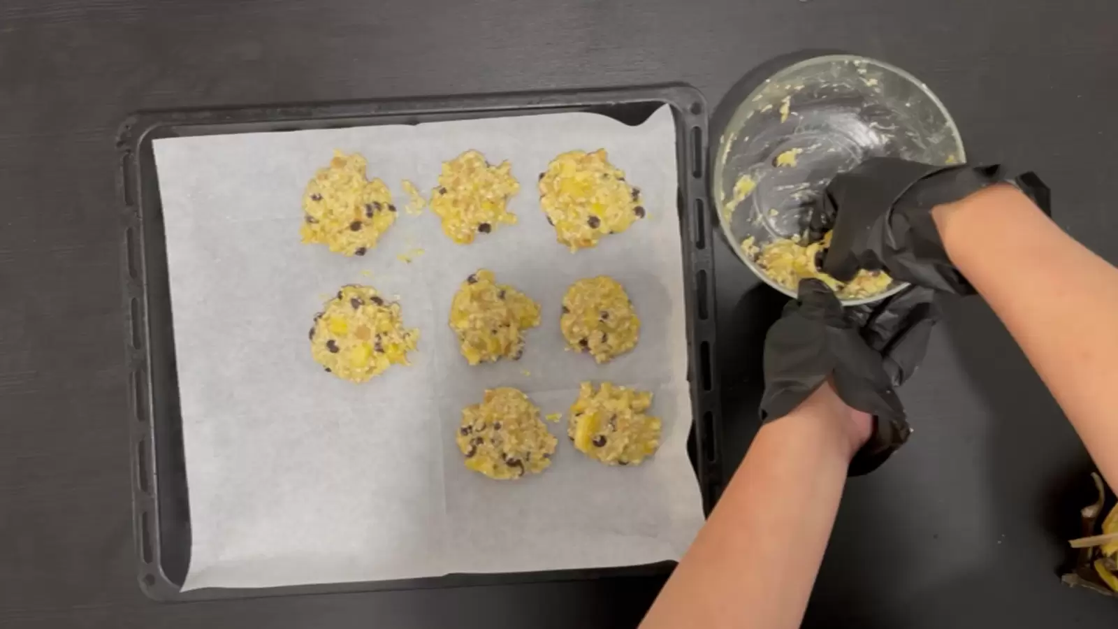 Bowl of banana and oatmeal cookie mix, baking sheet with parchment paper, and banana and oatmeal cookies