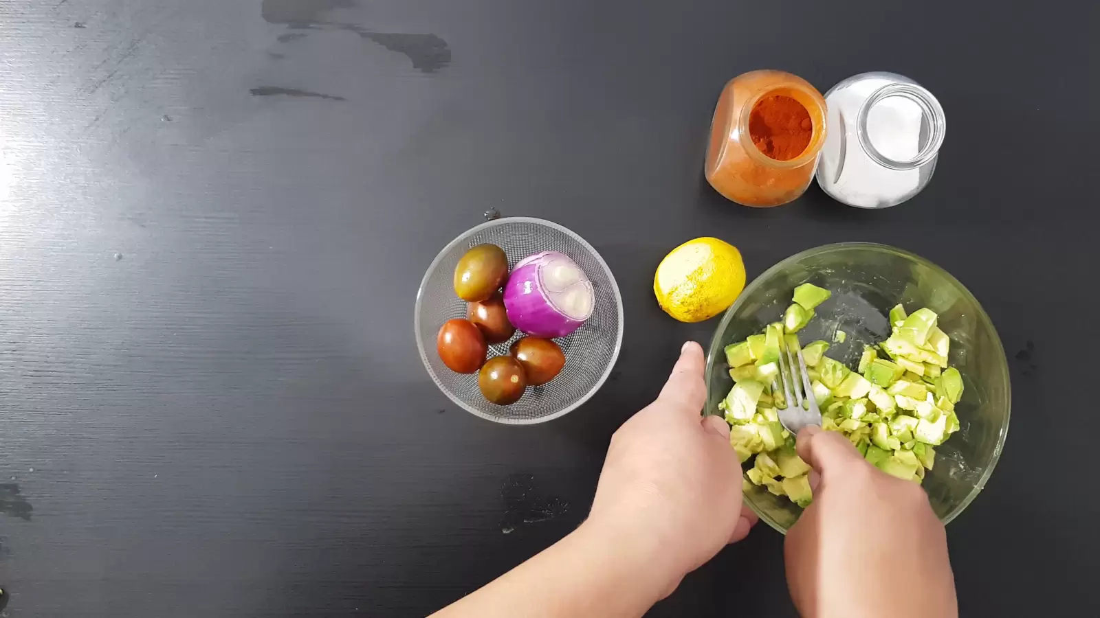 Spices, a bowl with tomatoes and onions, lemon fork mashed avocado in a bowl