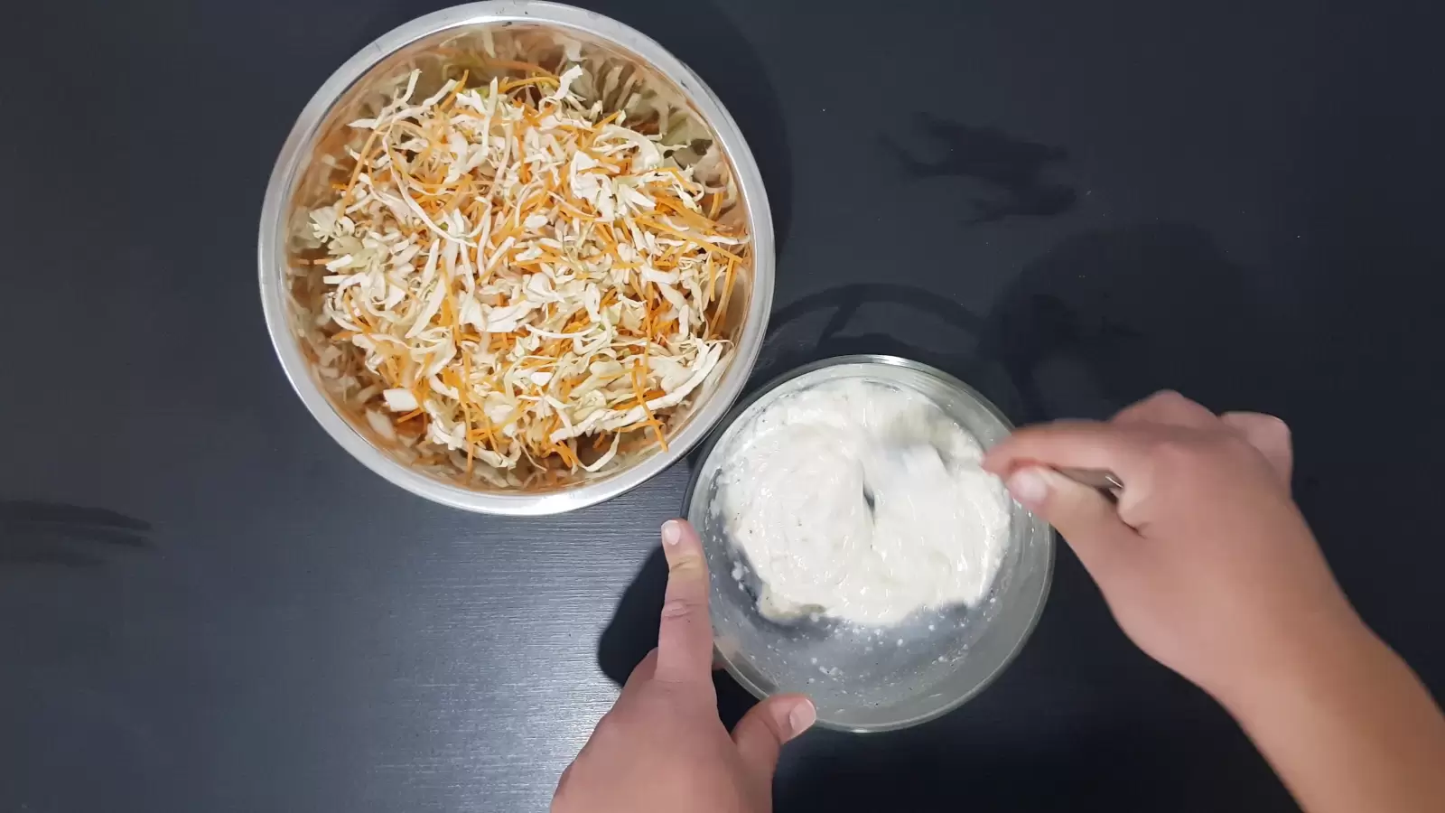 One bowl with cut carrots and cabbage, a fork stirs the mixture in the other bowl