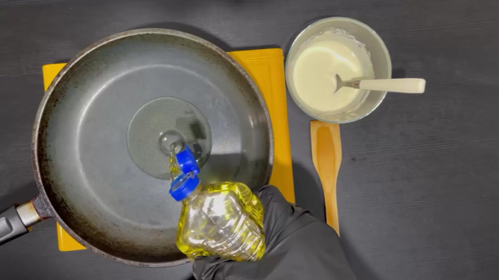 Bowl with batter, wooden spoon, bottle of oil poured into pan