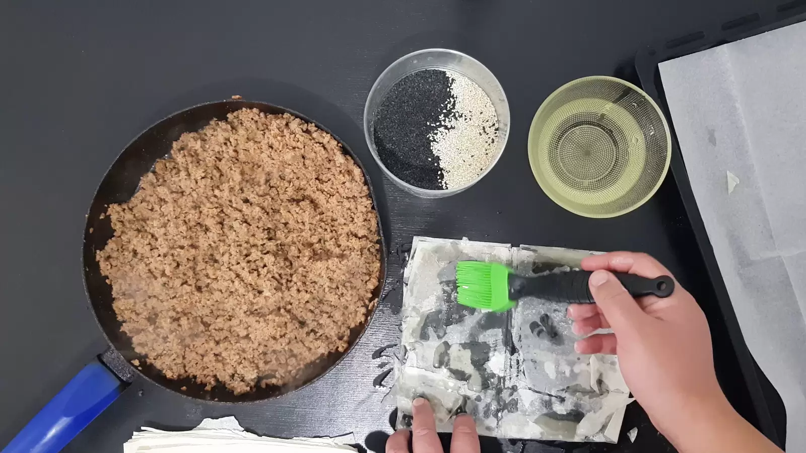 bowl with oil, bowl with white and black sesame, pan with beef, sheet of phyllo, brush