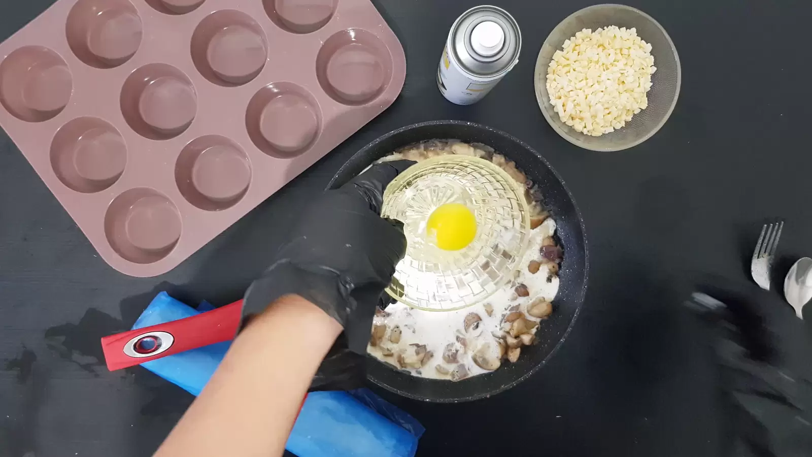 Bowl with cheese grated, bowl with egg, oil spray, spoon and fork, pan with mushrooms and cream, muffin tin, rolled filo dough