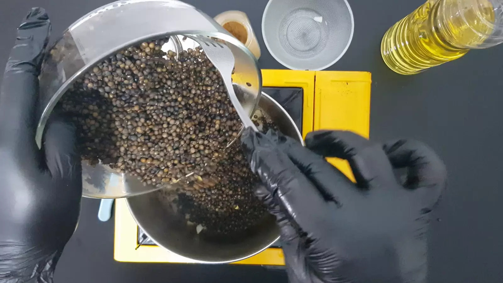 Bowl with lentils spilled into pot, empty bowl, jar of cumin, jar of oil, Gas stove