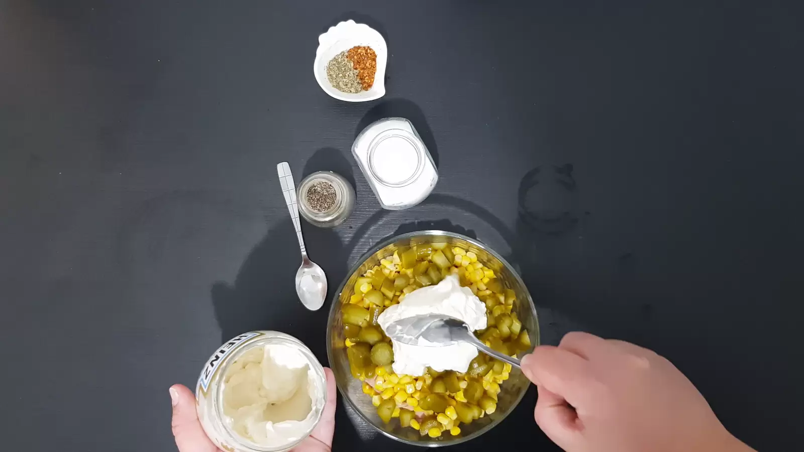 A jar of mayonnaise and a spoonful of mayonnaise in a bowl with corn, a bowl with chili, a jar of salt, a jar of black pepper