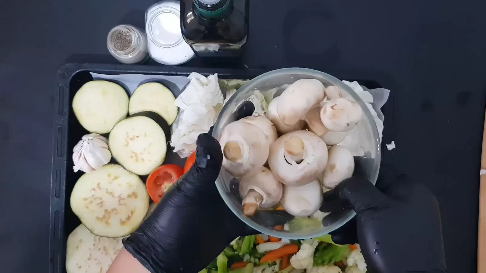 A bowl with mushrooms, a bottle of olive oil, a jar of salt, a jar of pepper.