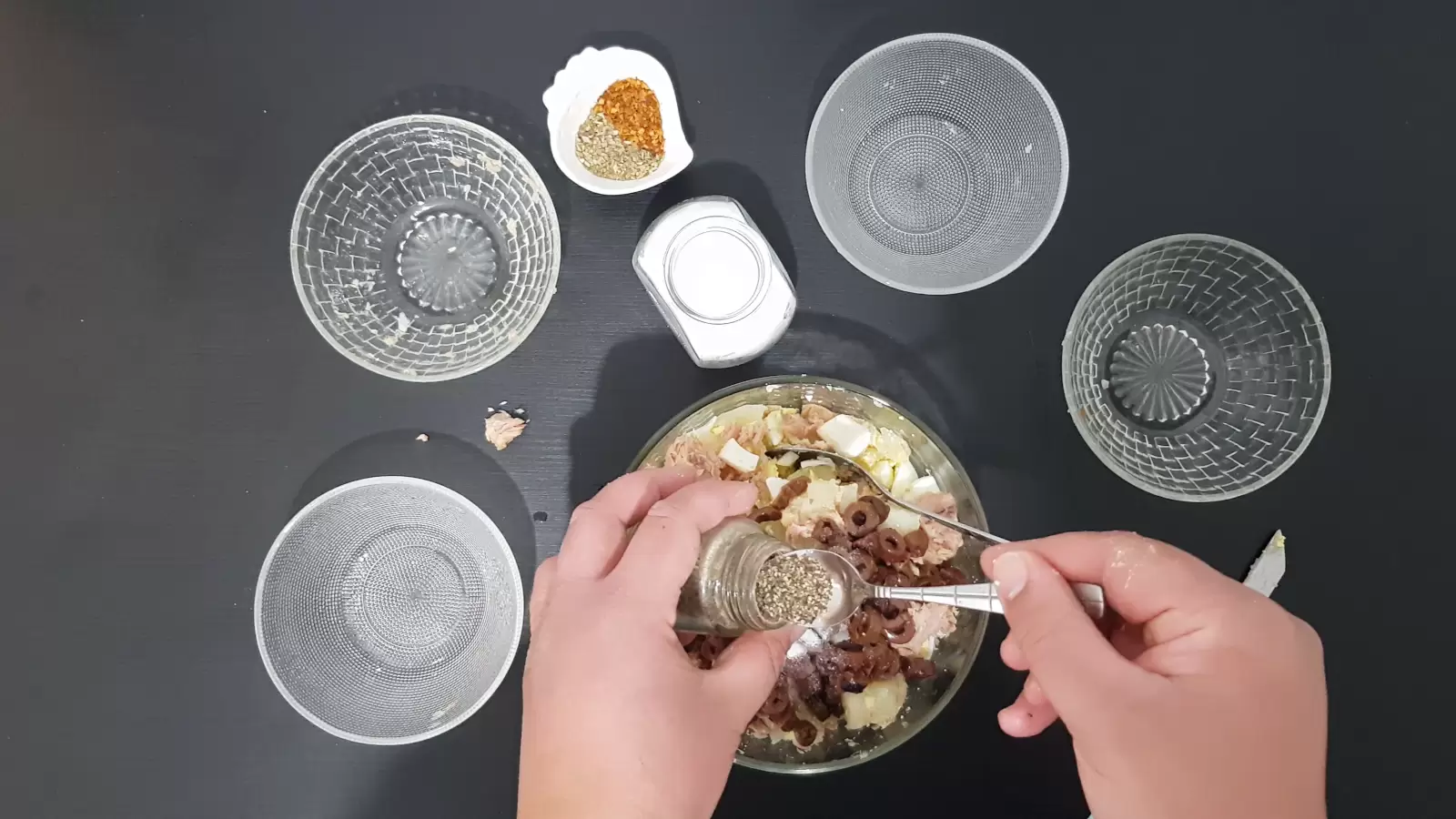 A bowl with olives, a jar of salt, a bowl with spices, a teaspoon of pepper, three empty bowls