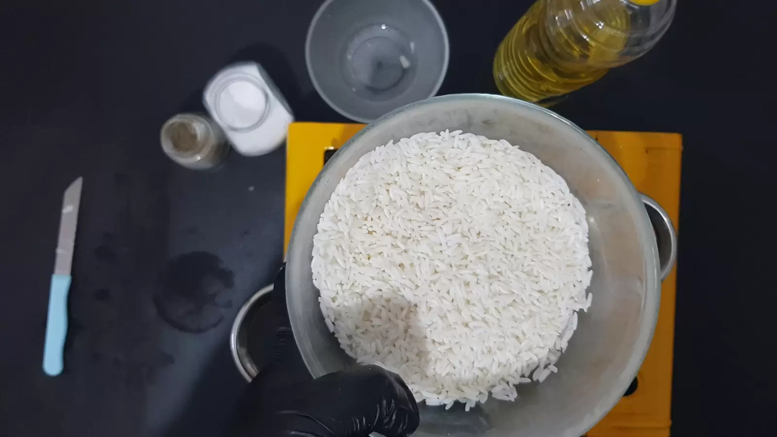 Oil, an empty bowl, a jar of salt, a jar of pepper, a bowl with rice, a knife