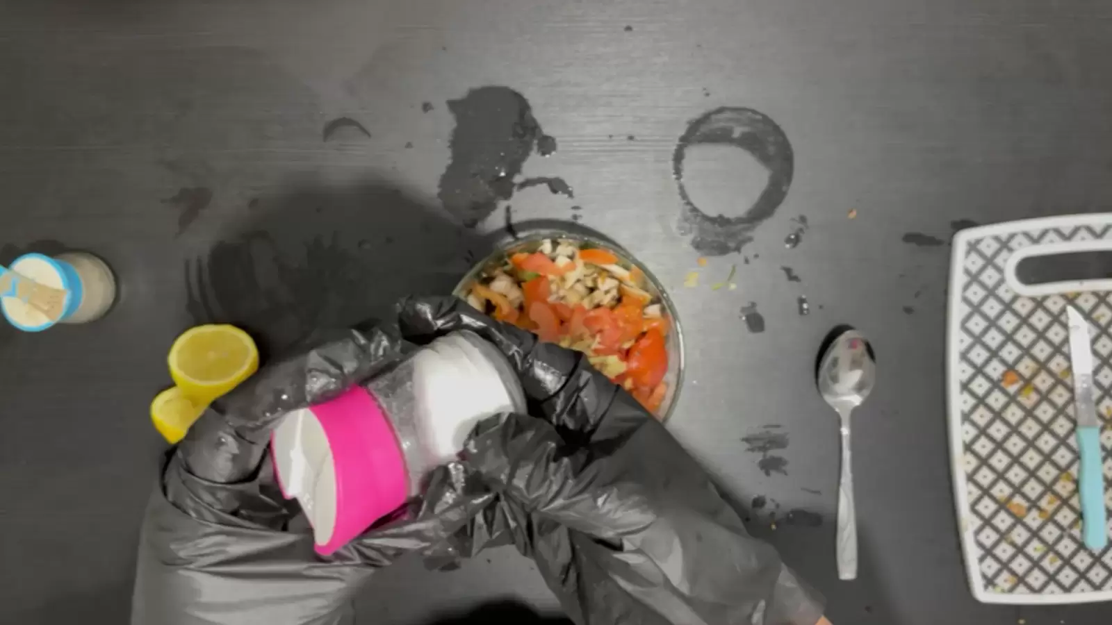 Bowl with lettuce, tomato and mushrooms, jar of salt, jar of pepper, cutting board and knife, spoon, lemon