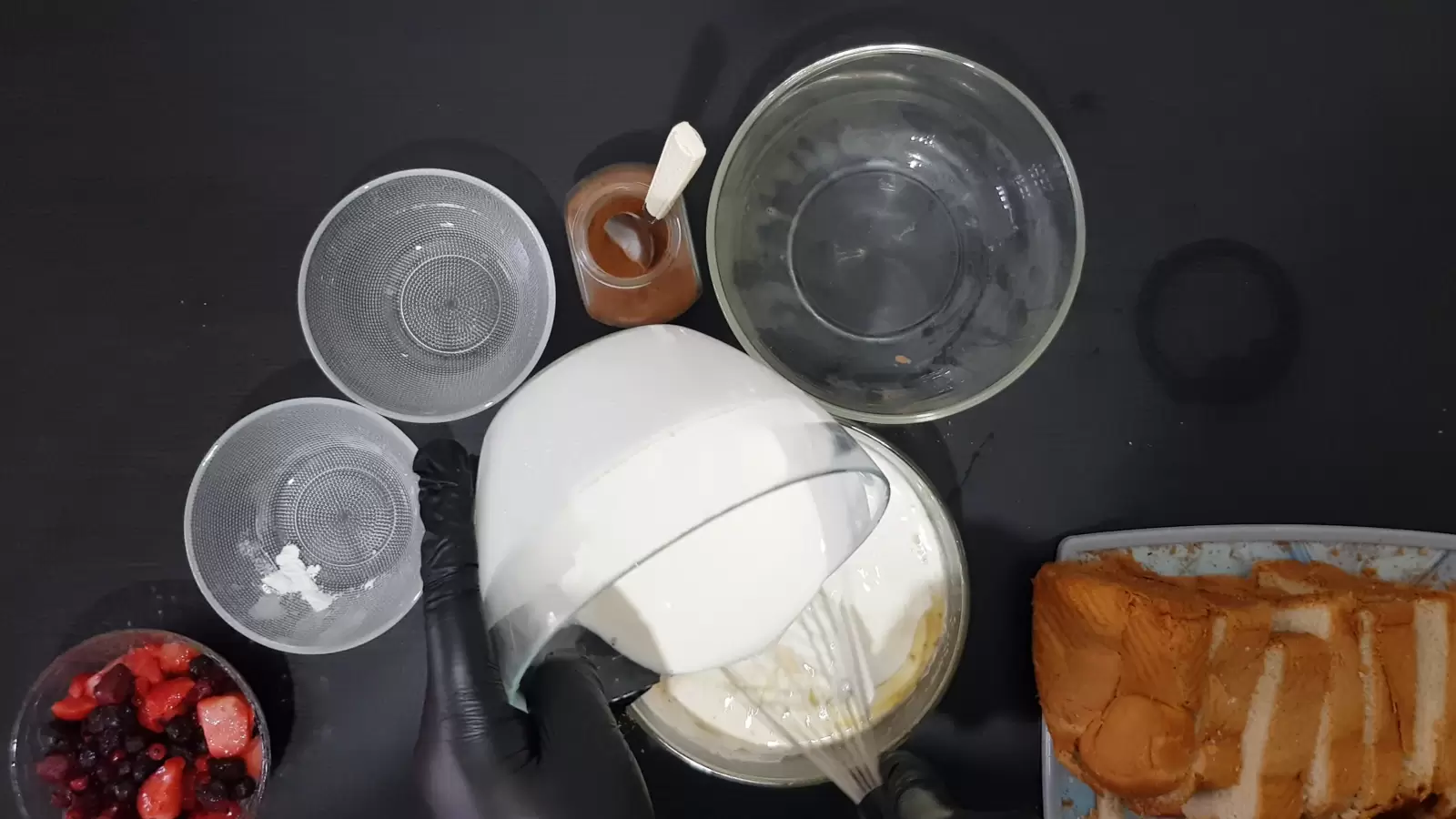 Sliced ​​bread on cutting board, sour cream poured into bowl with batter, 3 empty bowls, jar with cinnamon spice and spoon, bowl with berries and whisk