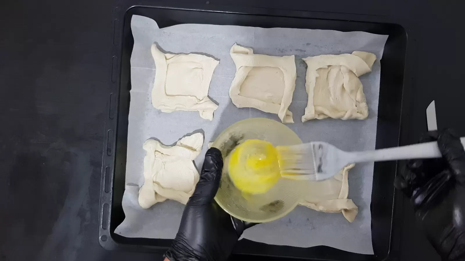 6 puff pastries ready on a baking sheet, bowl with egg and brush.