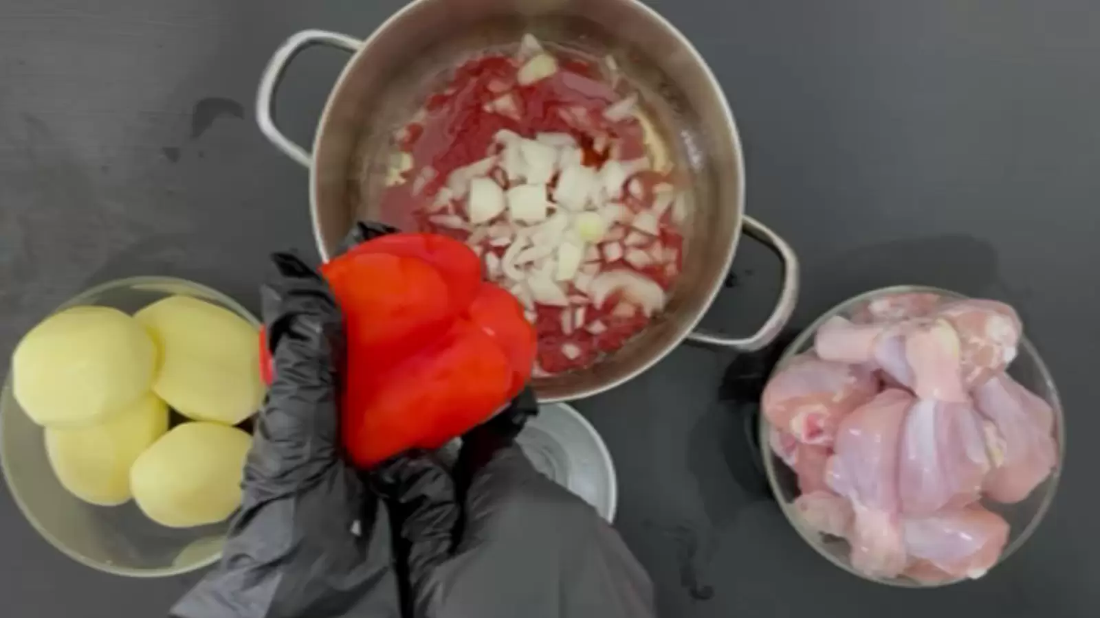 A bowl with chicken thighs, a bowl with 4 potatoes, a pot with tomato and onion sauce, a knife and red pepper