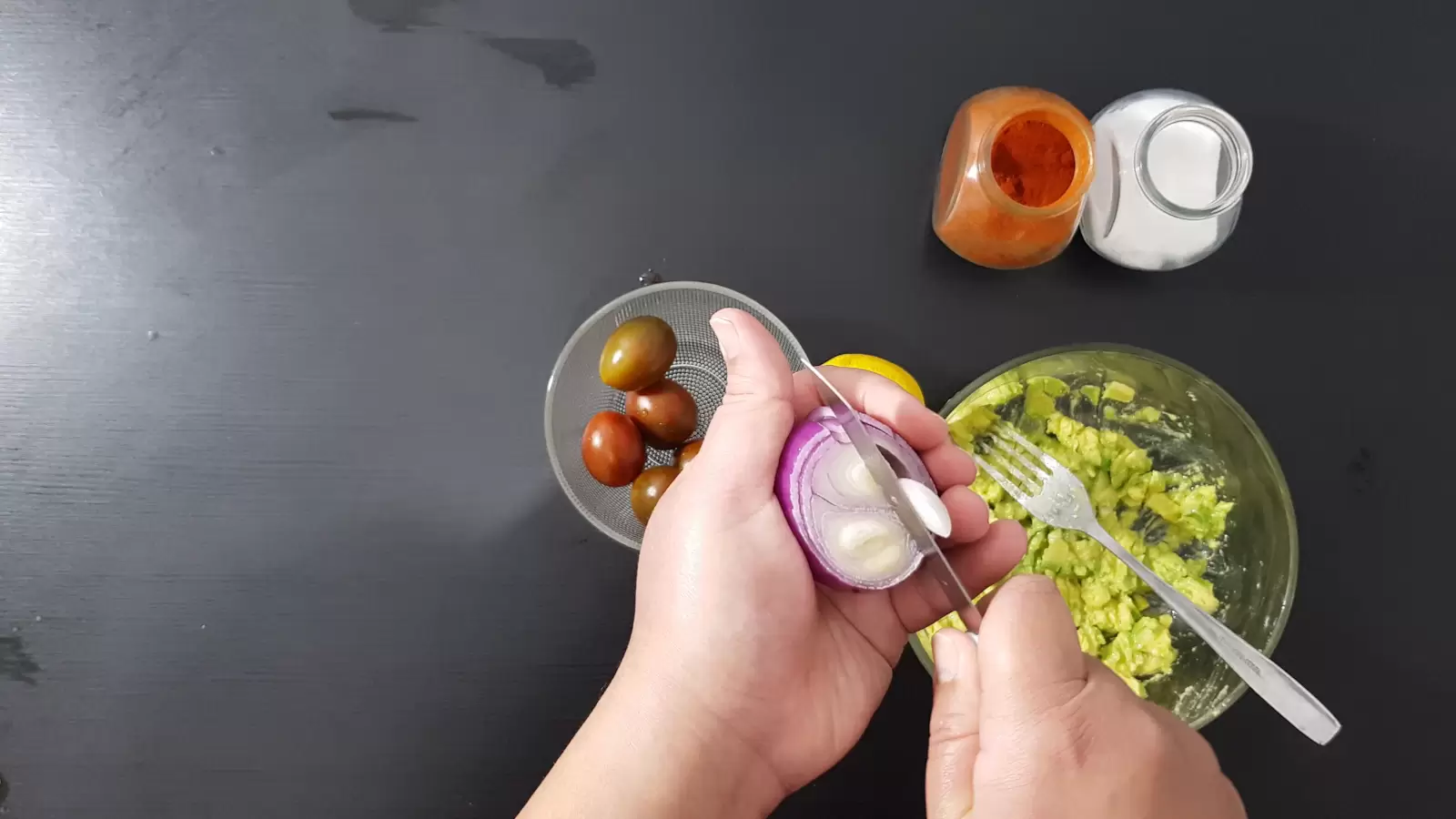 Spices, a bowl with tomatoes, mashed avocado in a bowl, a knife cutting a purple onion