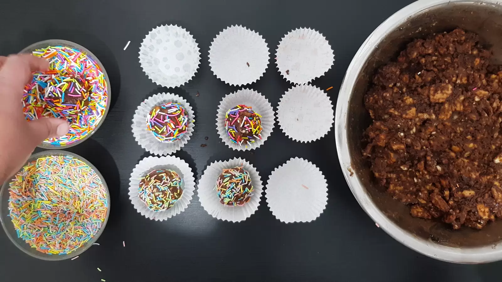 Chocolate balls, bowl with mixture, baking cups, rainbow sprinkles