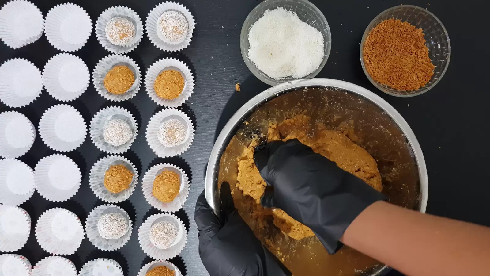 A bowl of ball mix, a bowl of caramelized coconut, a bowl of coconut, milk jam balls and biscuits on baking paper